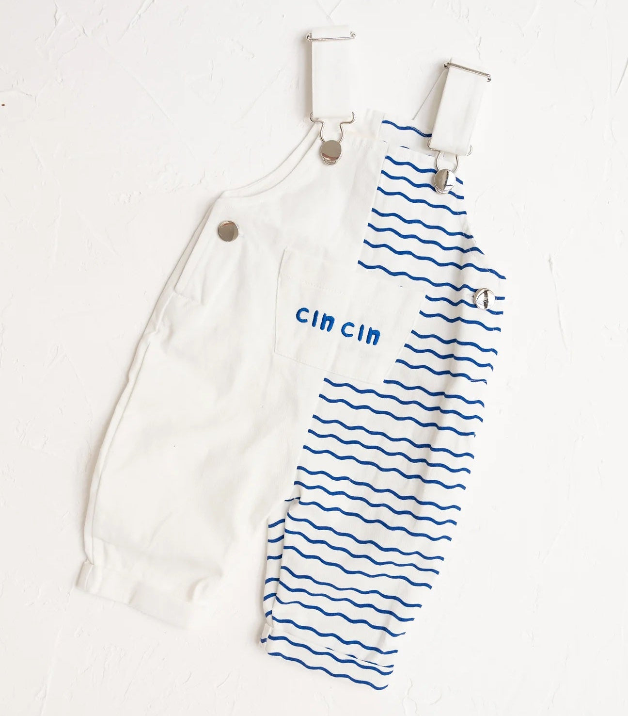 Two baby rompers, one white with 'cin cin' text and the other blue with wavy pattern, hanging on a white background.