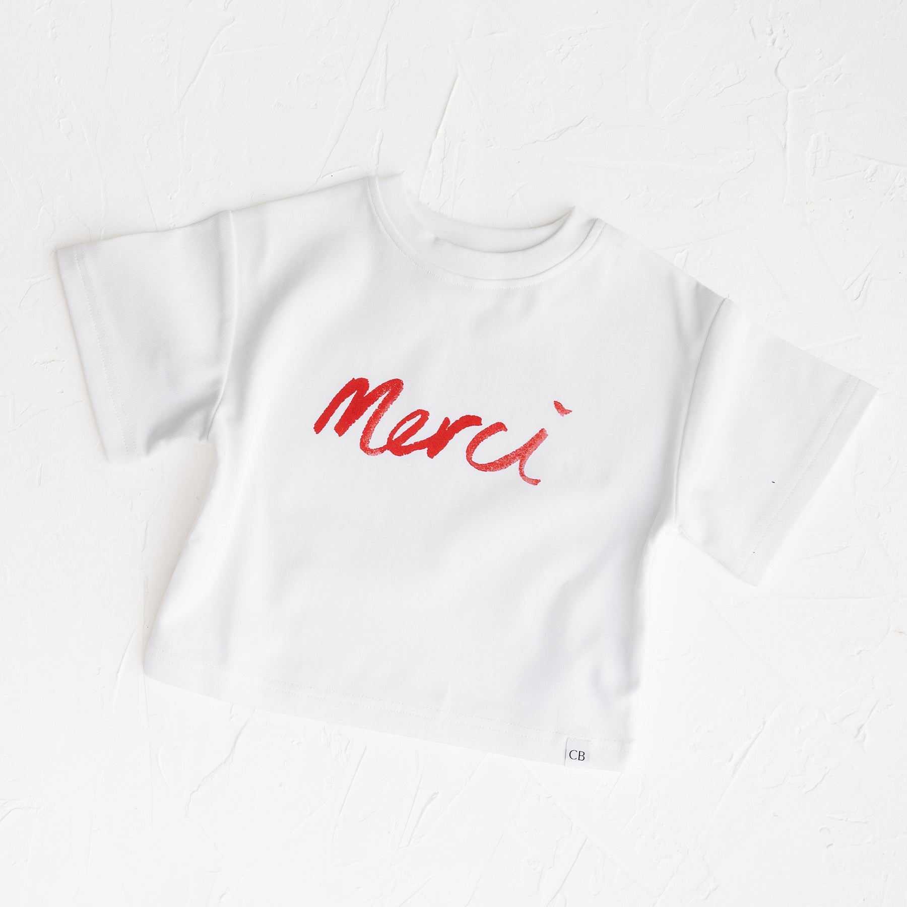 White t-shirt with red 'Merci' text on a white background