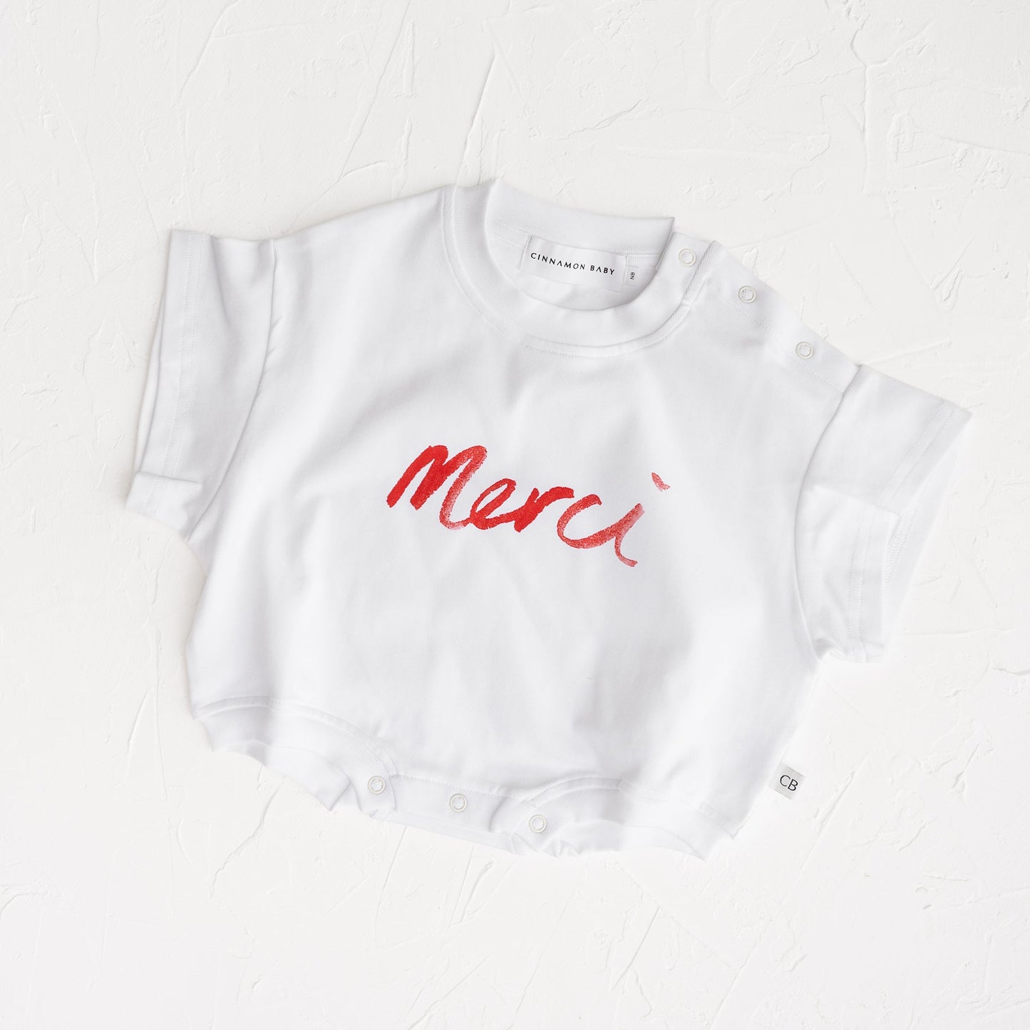 White t-shirt with red 'Merci' text on a white background