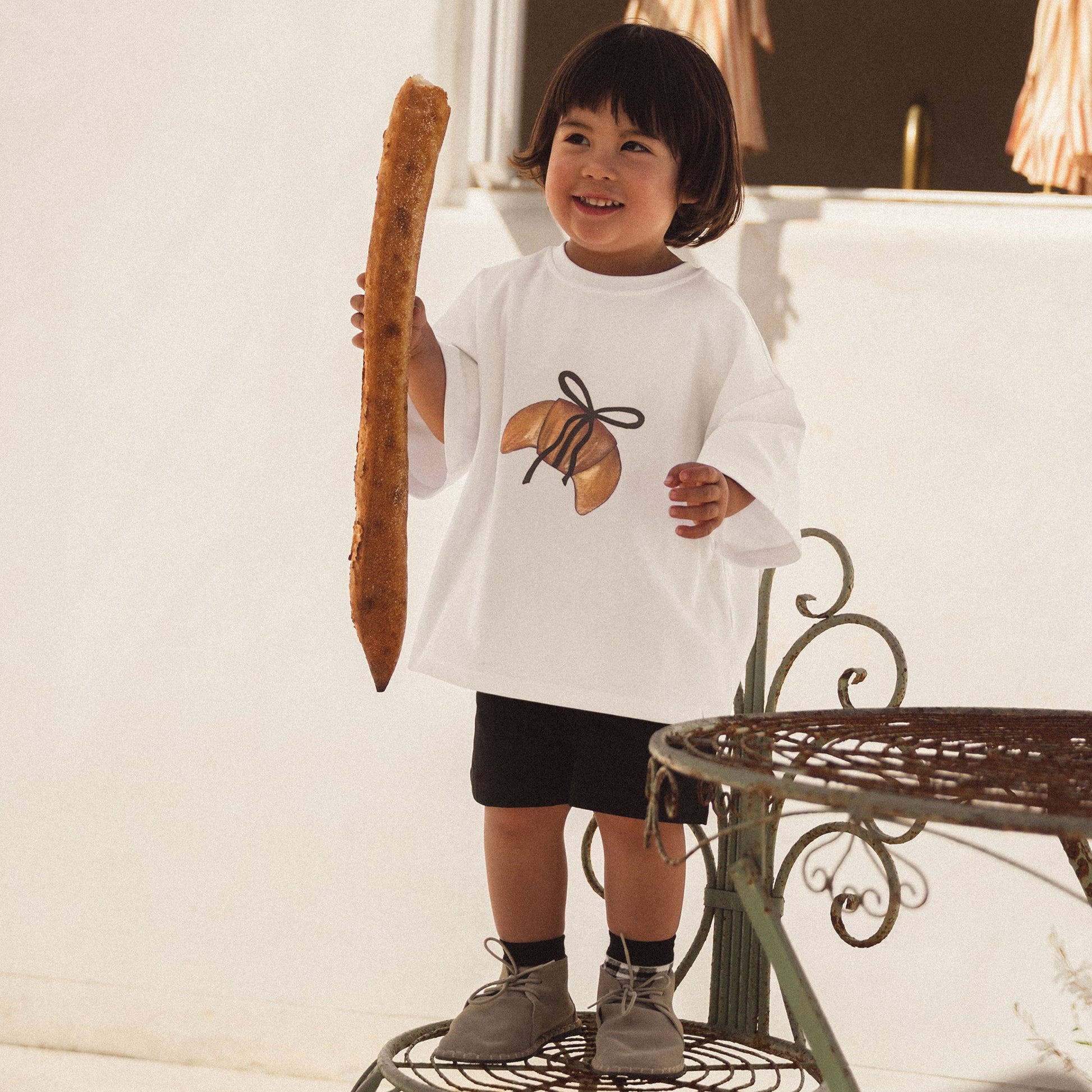 Child holding a large bread roll indoors with curtains in the background
