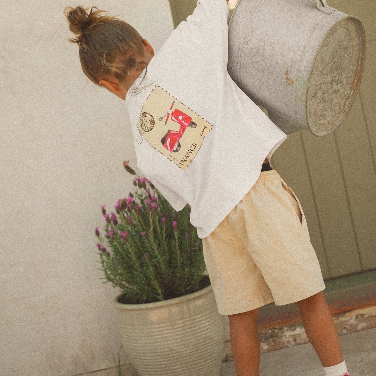 Child holding a watering can near a potted plant on a patio