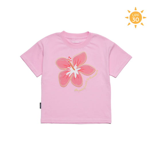 A light pink short-sleeve t-shirt with a large pink hibiscus flower graphic on the front, featuring a small gold script and a black tag on the side, shown on a white background with a yellow UPF 30 sun icon in the top right corner.