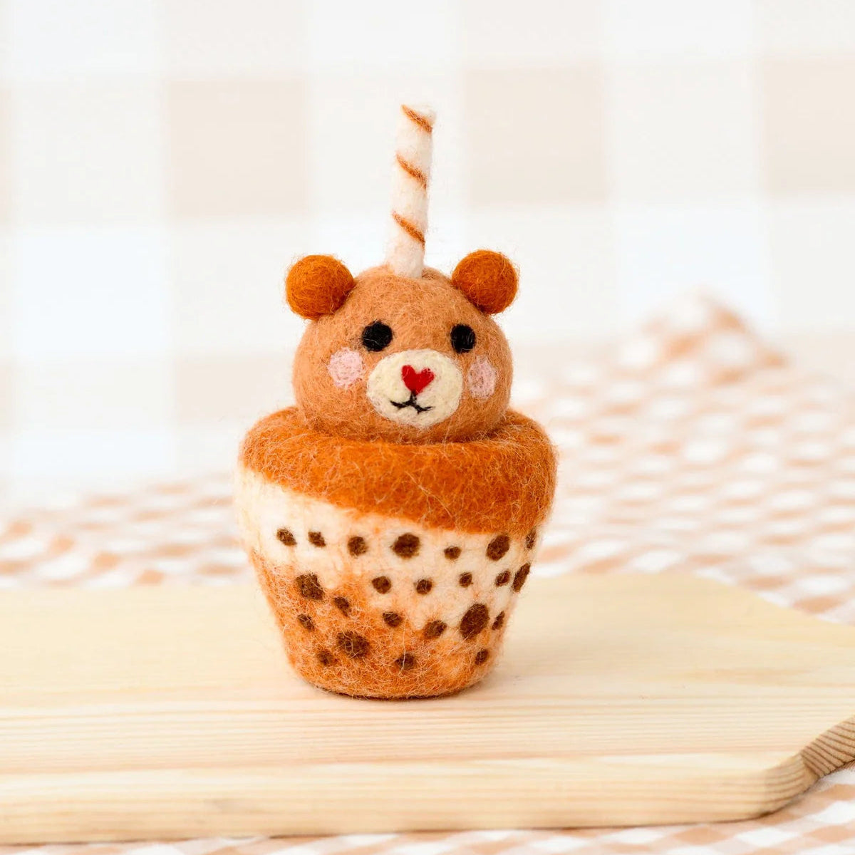 Plush toy resembling a bear in a cup with polka dot pattern on a wooden surface.