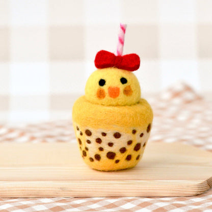 Yellow cupcake with a chicken design and red bow on a wooden board.