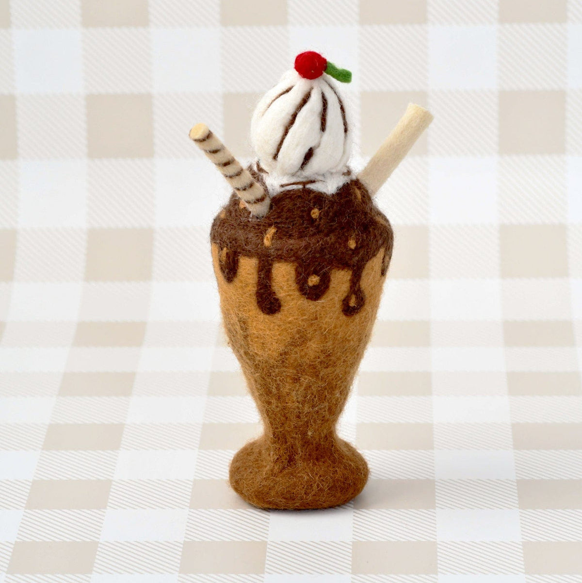 Felted ice cream cone with chocolate sauce and a cherry on top against a checkered background