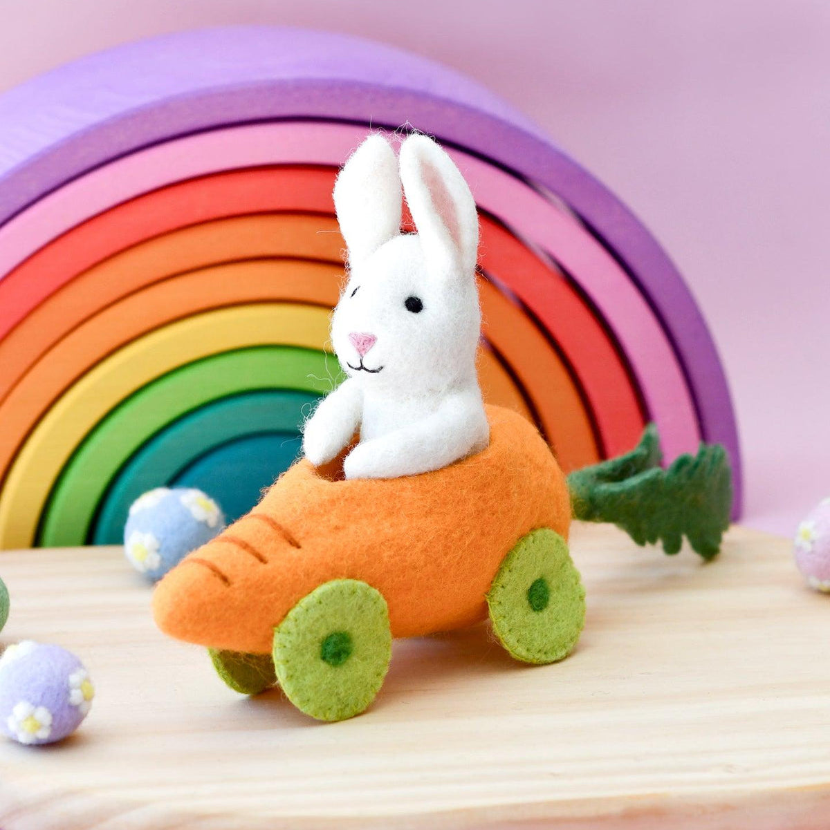 Toy rabbit in a carrot car with a rainbow and wooden rings in the background