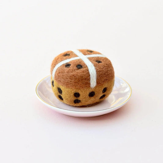 Felted hot cross bun on a white plate with a white background
