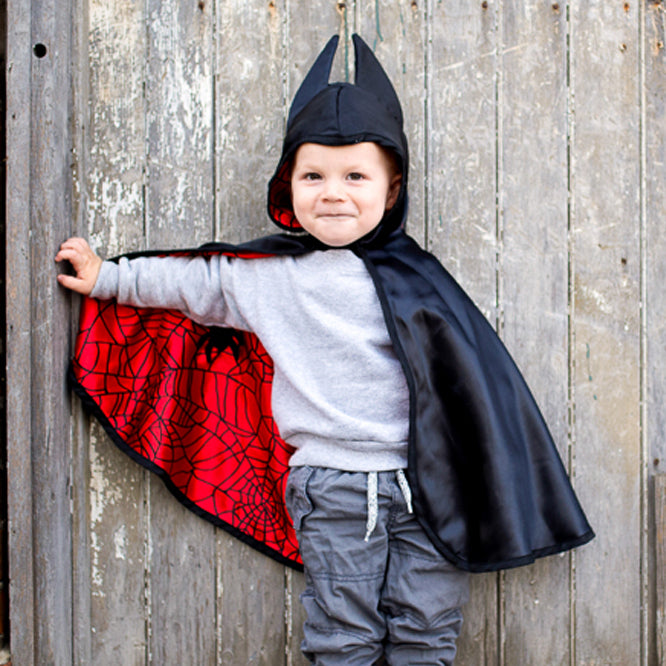 Child wearing a black and red superhero cape against a wooden background