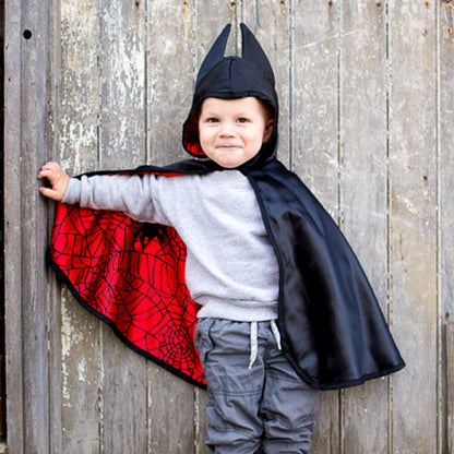 Child wearing a black and red superhero cape against a wooden background