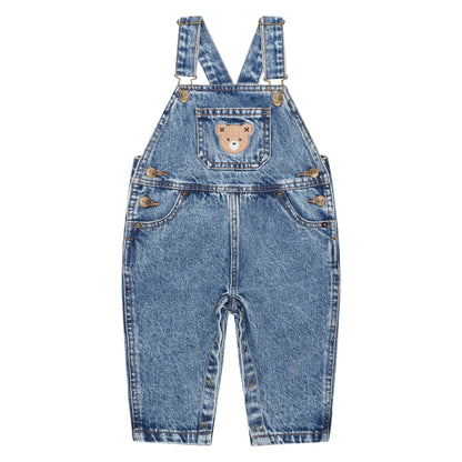 Blue denim overalls with a teddy bear patch on a light pink background