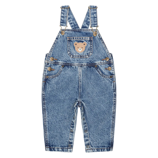 Blue denim overalls with a teddy bear patch on a light pink background