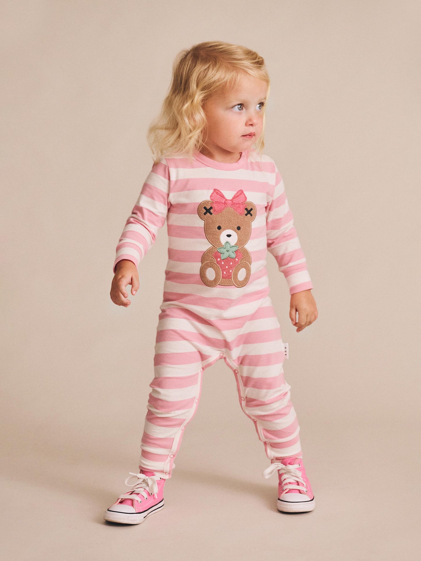 Child wearing a pink and white striped outfit with a teddy bear design on a beige background