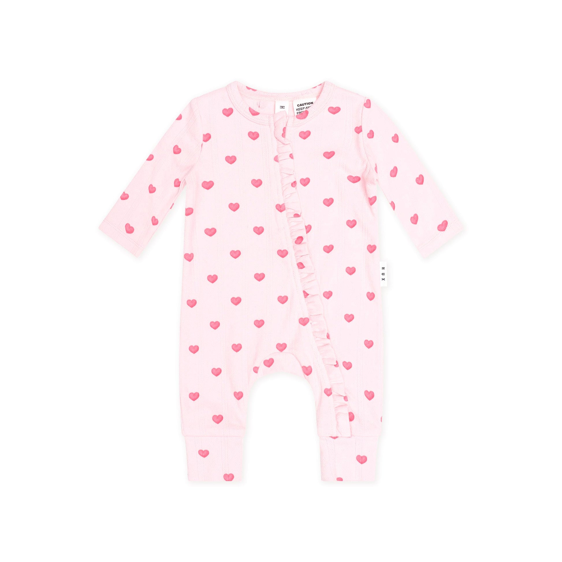 A light pink baby footless one-piece romper with long sleeves, ruffle trim along the front, and an allover pattern of small pink hearts, shown on a plain white background.