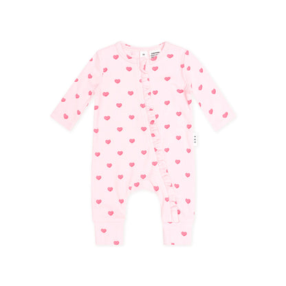 A light pink baby footless one-piece romper with long sleeves, ruffle trim along the front, and an allover pattern of small pink hearts, shown on a plain white background.
