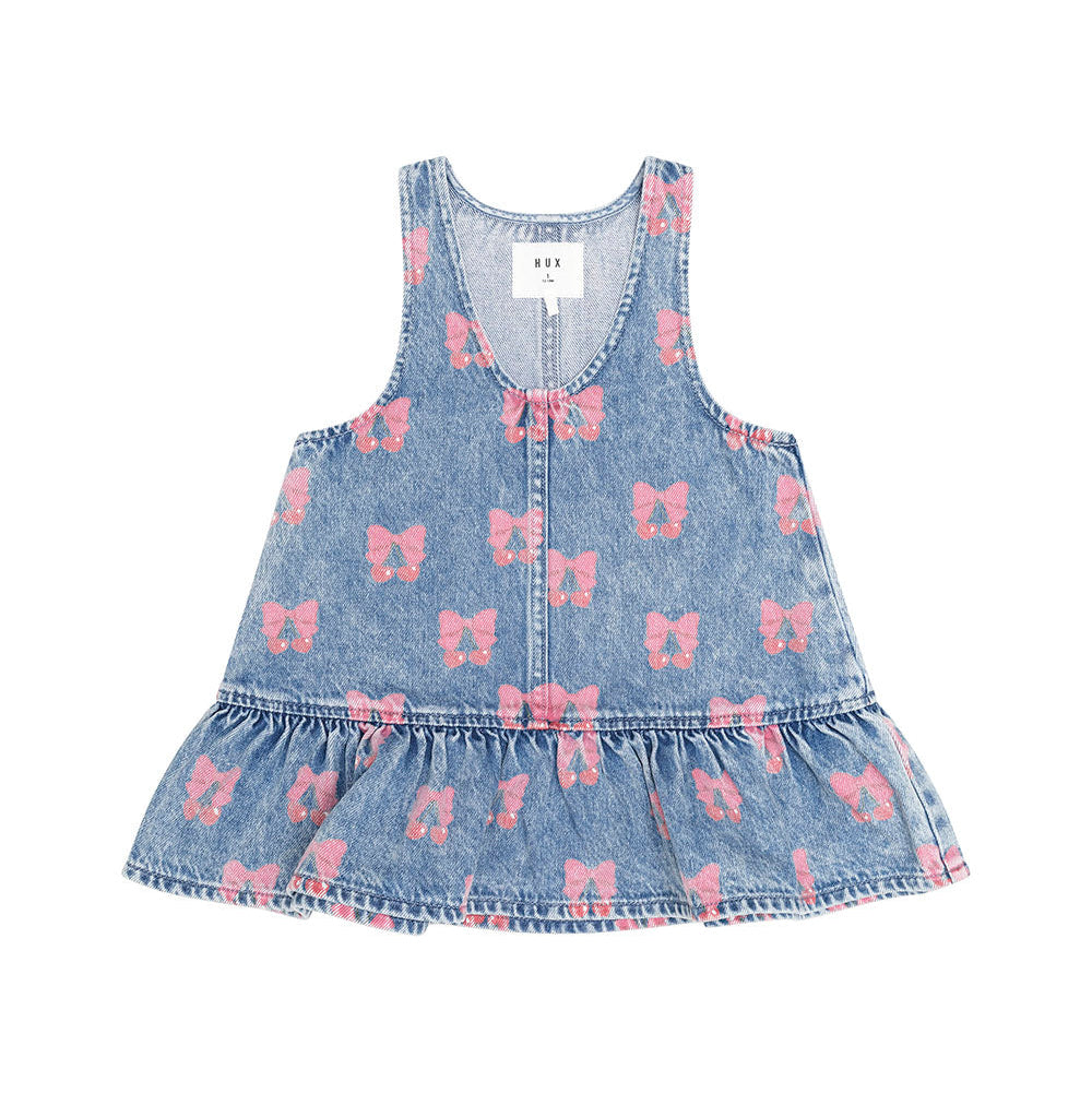 A sleeveless light blue denim dress for toddlers, featuring a pink bow pattern and a ruffled hem, shown flat on a white background.