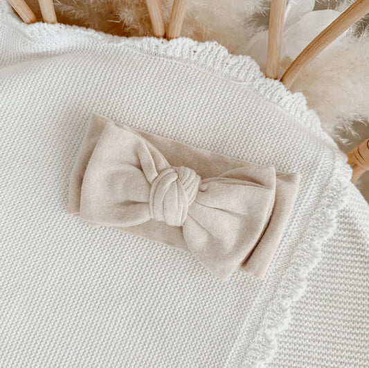 Beige bow headband on a textured white surface