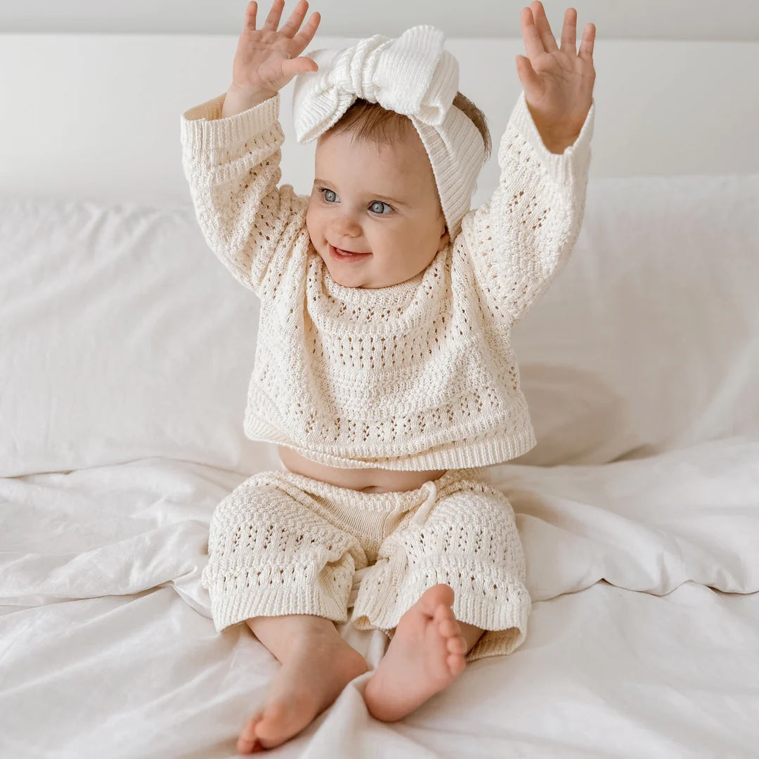 Baby in a white knit outfit with a matching headband on a white background