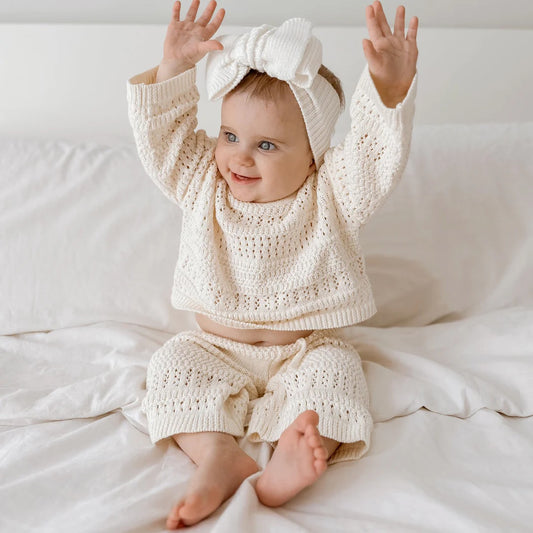 Baby in a white knit outfit with a matching headband on a white background