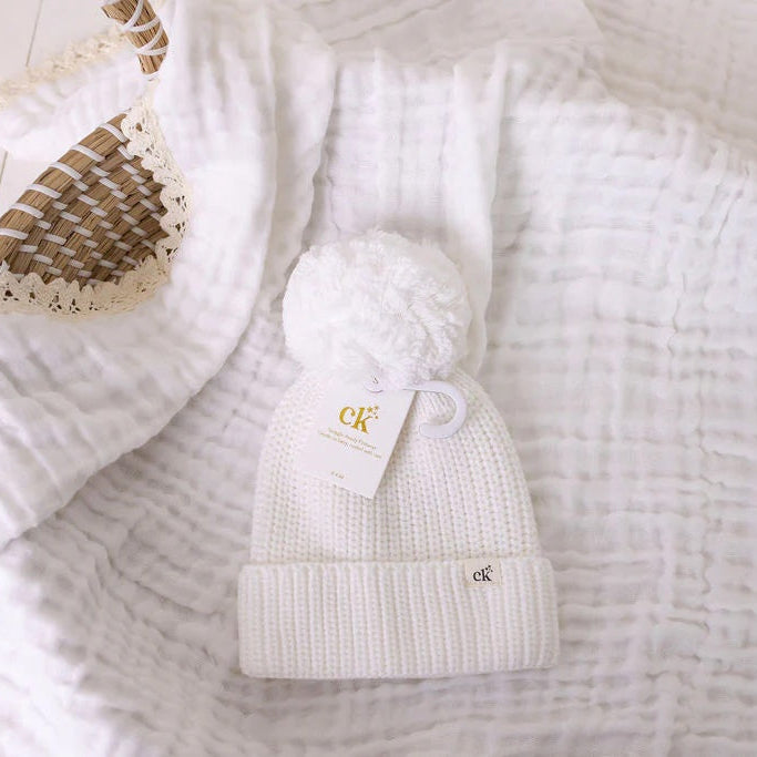 White knit beanie with a logo on a textured white surface