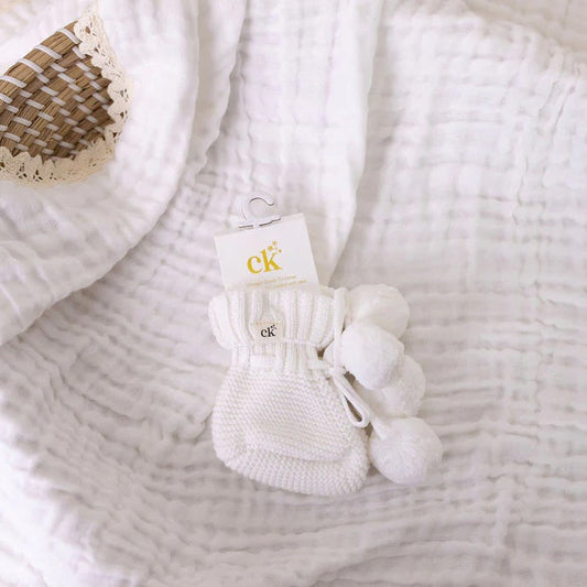 White textured blanket with a small basket and white socks on top, featuring the brand 'CK'.