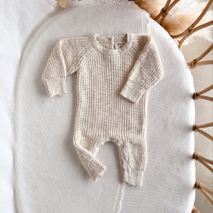Knitted baby romper on a textured surface with a wicker chair in the background
