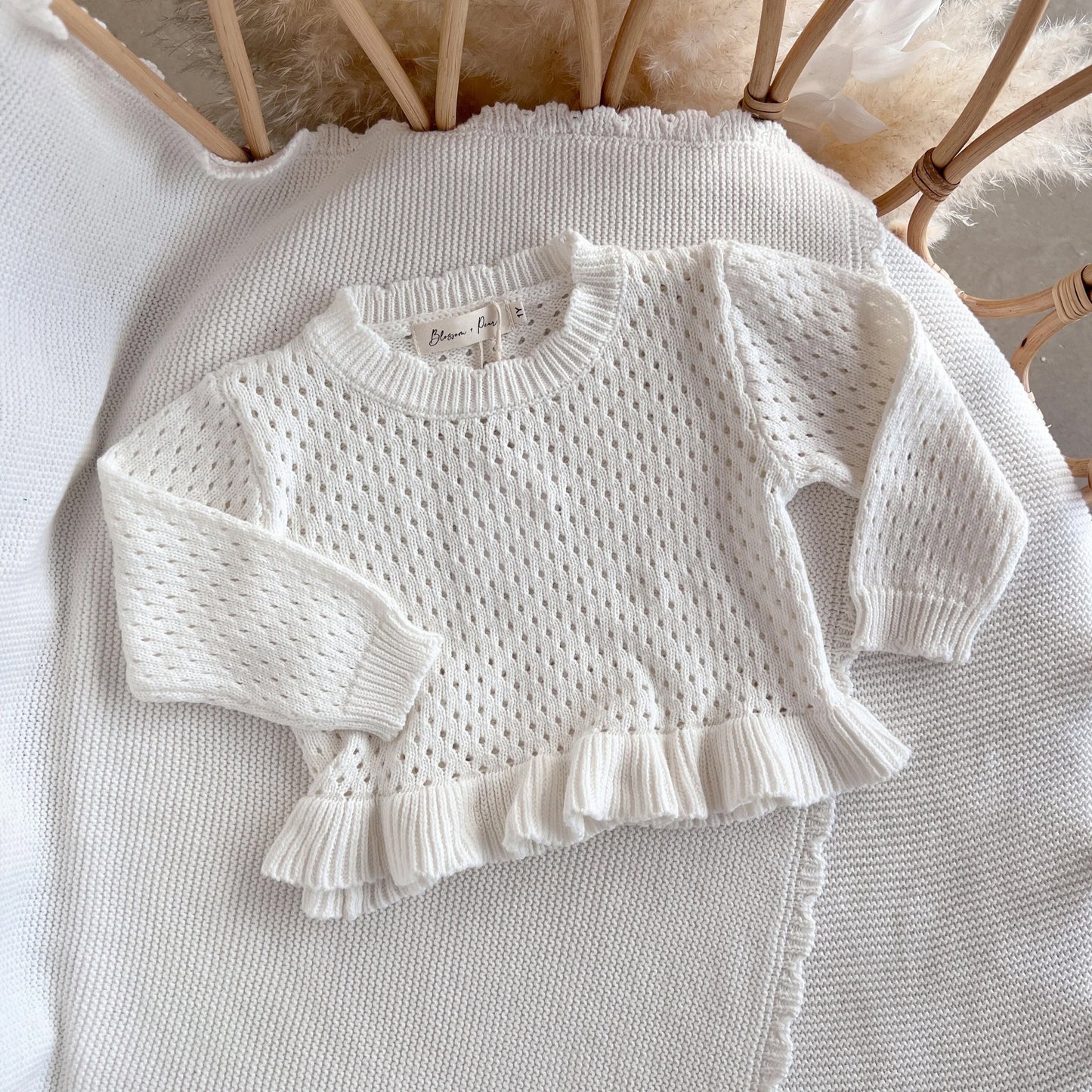 White knitted sweater with ruffled details on a textured surface