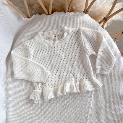 White knitted sweater with ruffled details on a textured surface