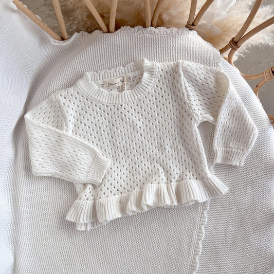 White knitted sweater with ruffled details on a textured surface