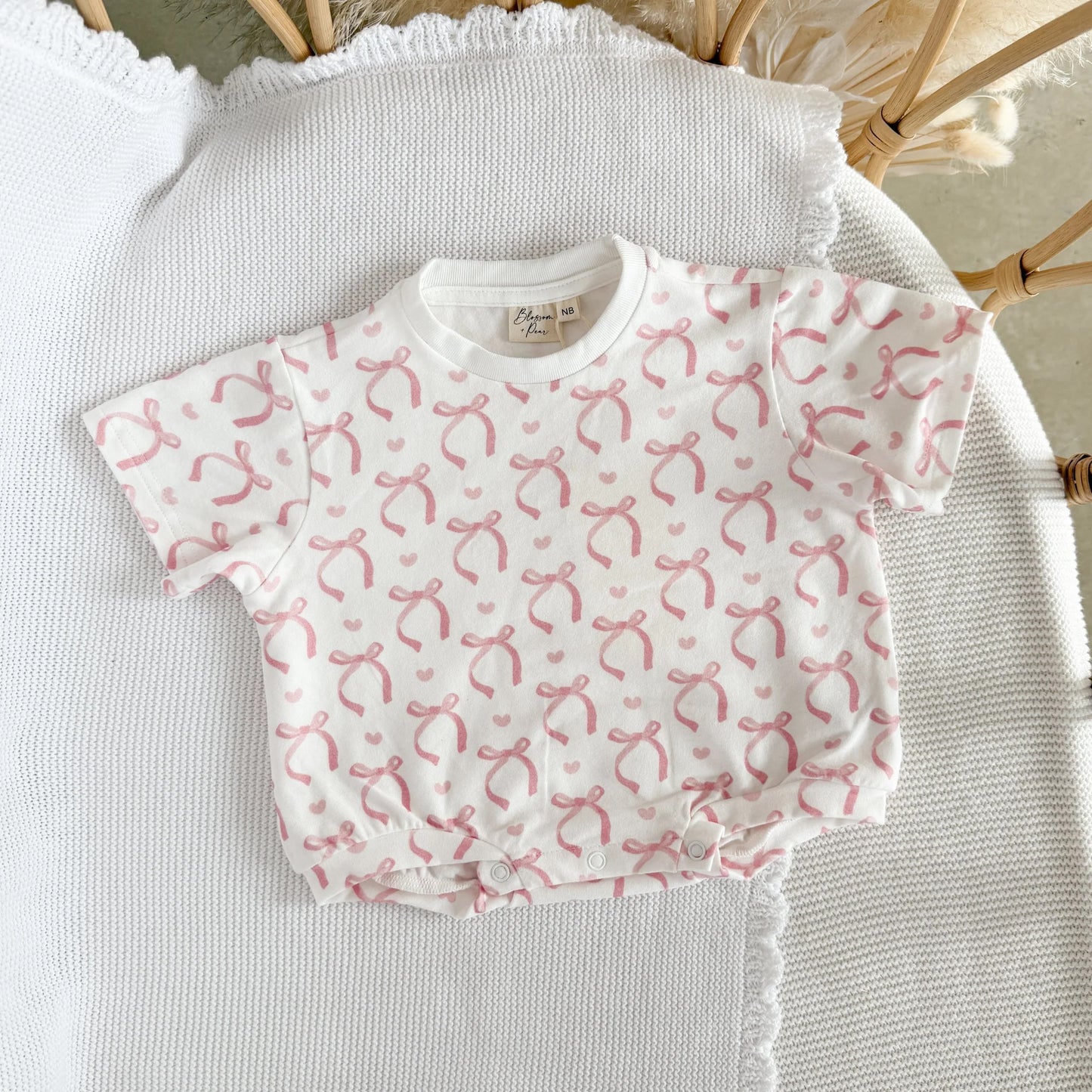 Baby romper with pink bow pattern on a textured surface