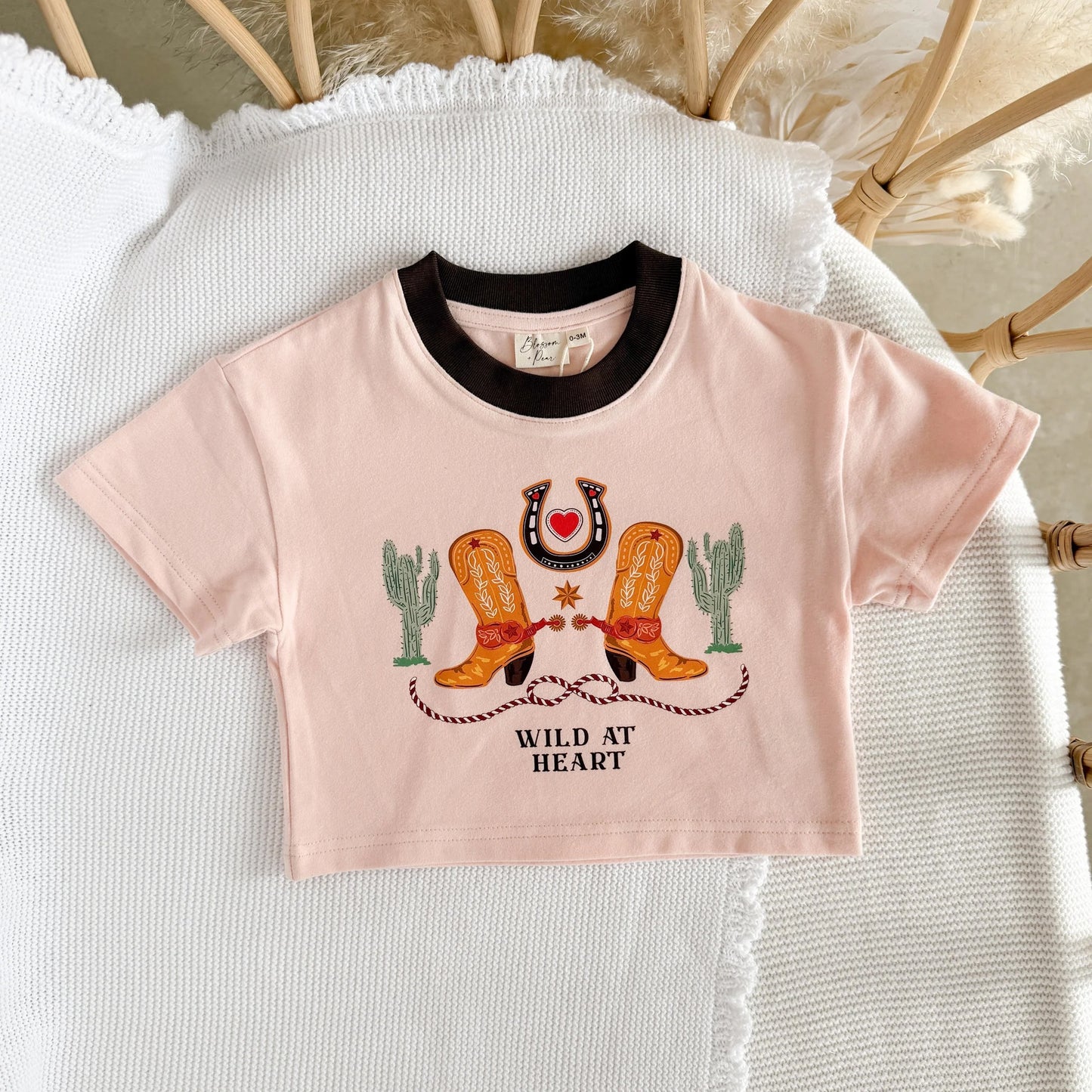 Pink crop top with cowboy boot and cactus design on a textured white surface