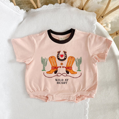 Pink baby romper with cowboy boots and cactus design on a textured surface