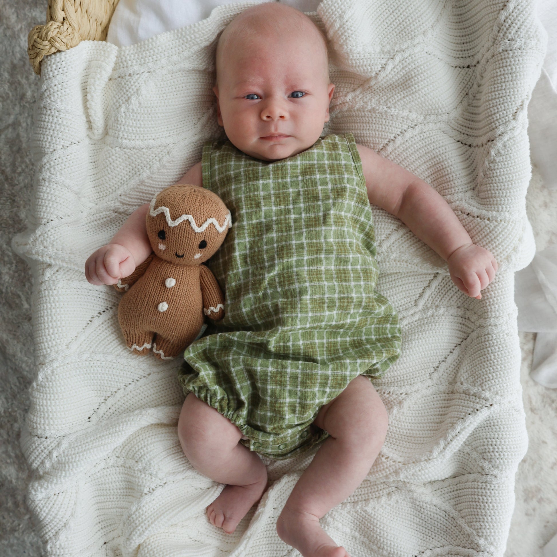 Baby in a green romper with a gingerbread toy in a woven basket