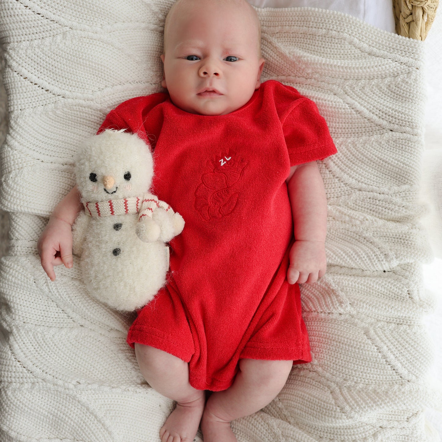 Baby in a red outfit holding a plush toy on a textured blanket