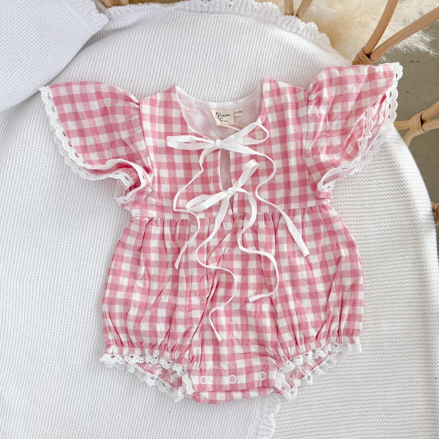 Pink and white checkered baby romper with ruffled details on a white surface.