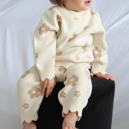 Child wearing a cream-colored outfit with floral patterns on a white background