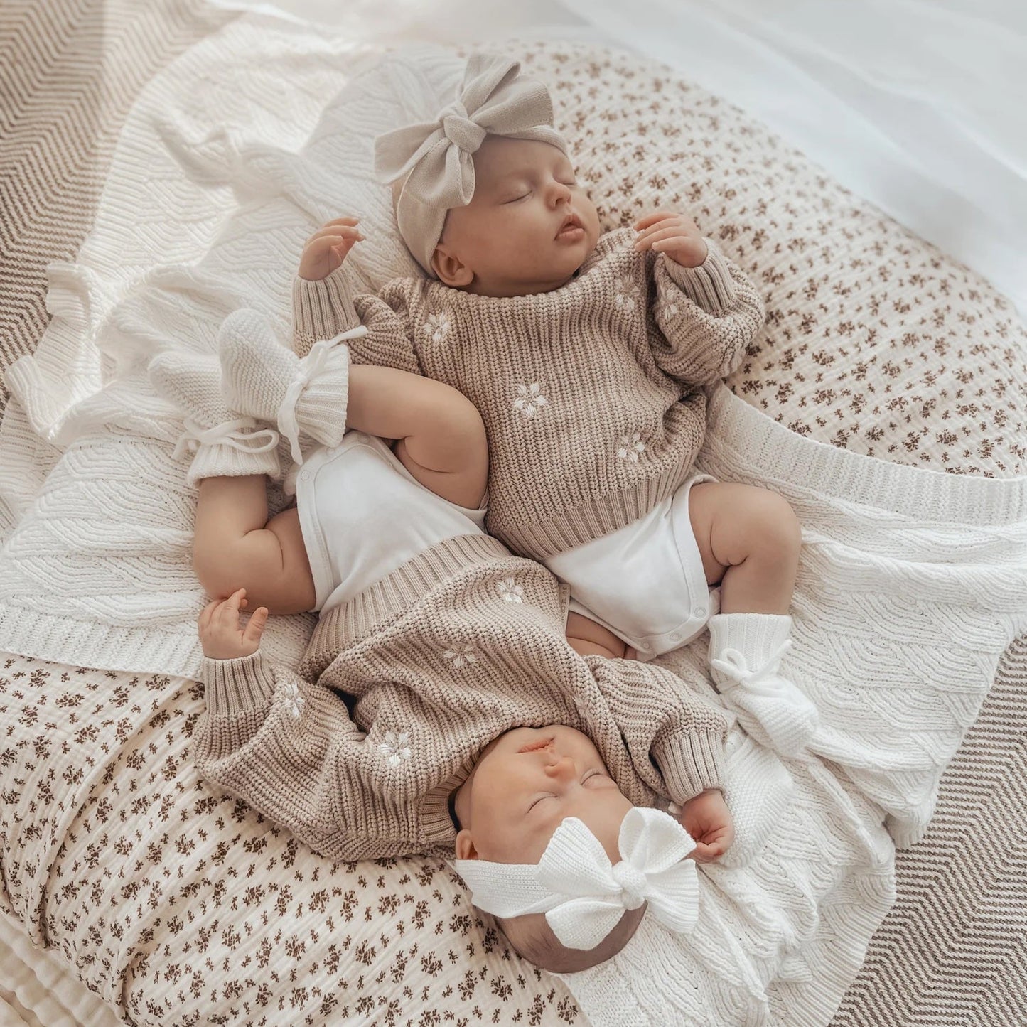 Two babies in matching outfits with bows, lying on a textured blanket.