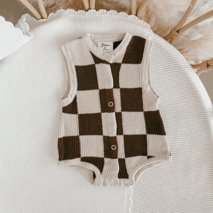 Checkered baby romper on a textured surface with blurred background