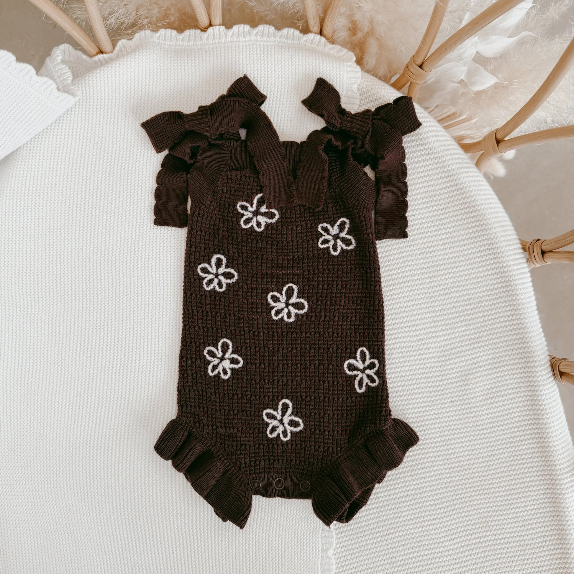 Brown baby romper with white flower patterns on a white surface