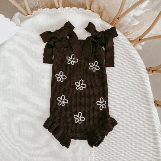Brown baby romper with white flower patterns on a white surface