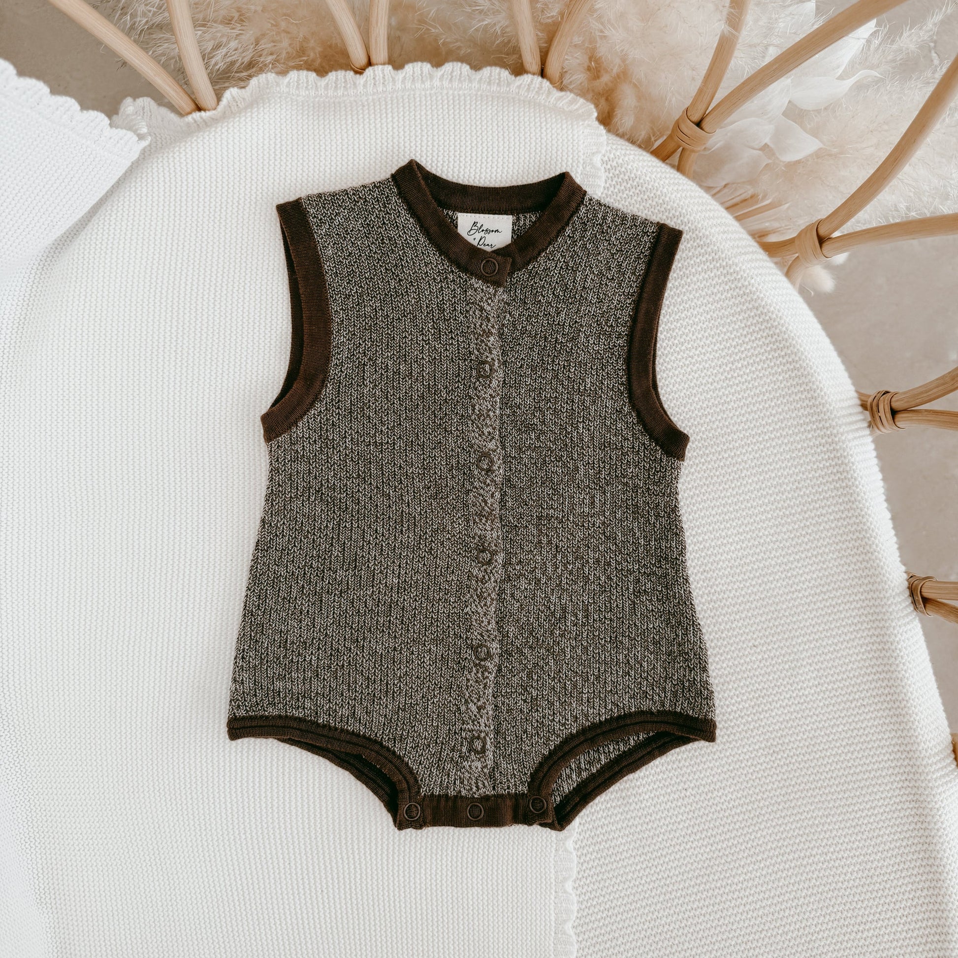 Textured baby romper with brown trim on a white surface