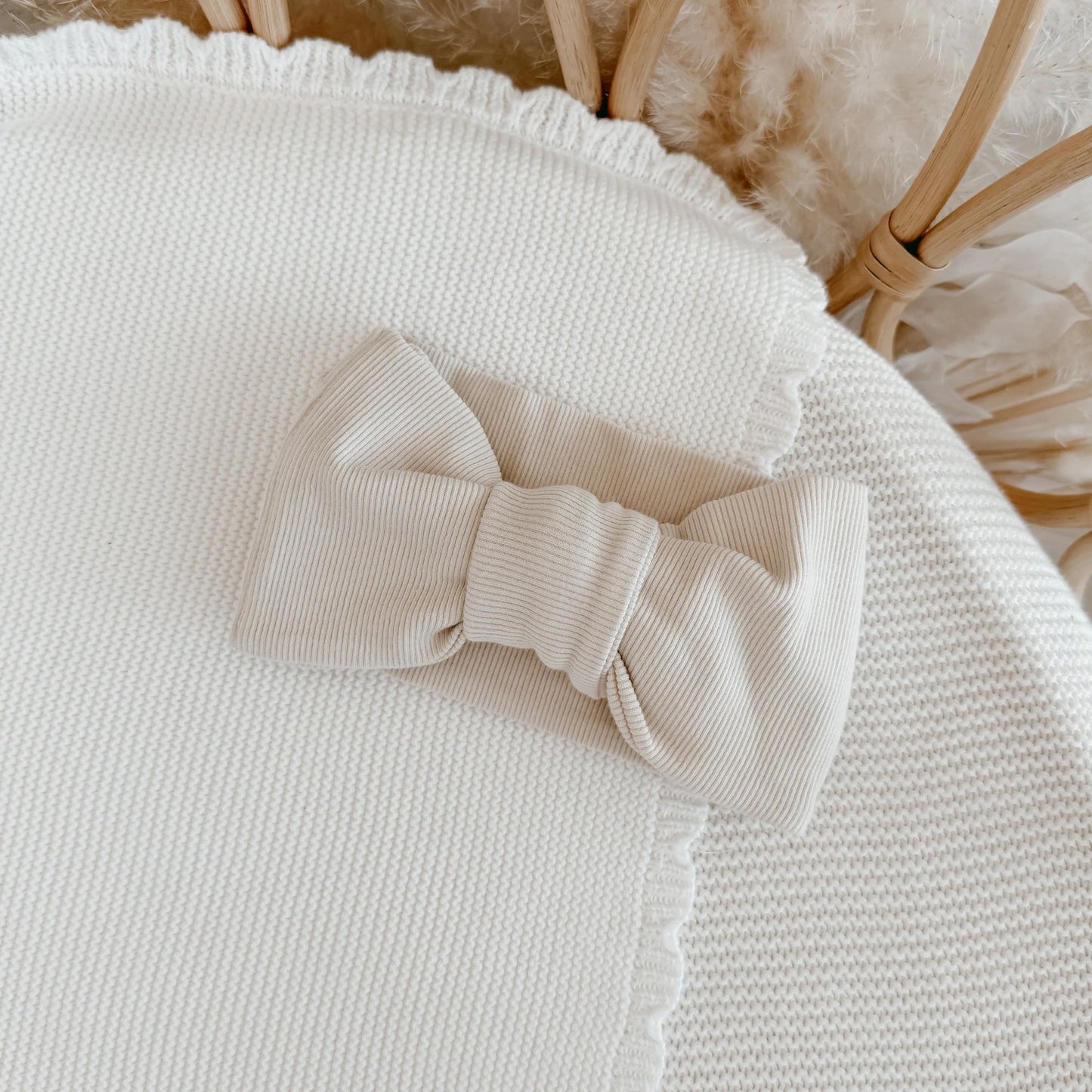 Beige knitted bow on a textured surface with a wicker basket in the background