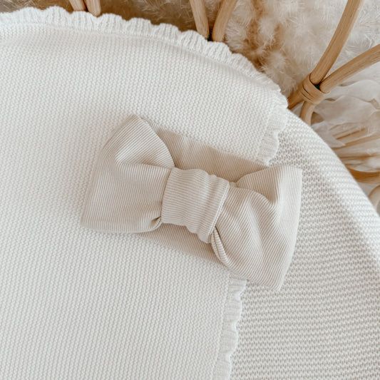 Beige knitted bow on a textured surface with a wicker basket in the background