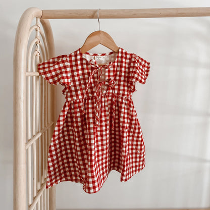 Red and white checkered dress on a wooden hanger against a neutral background