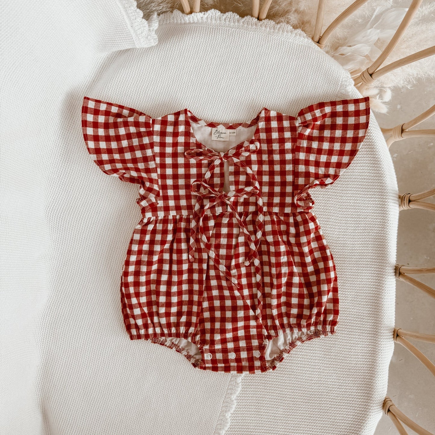 Red and white checkered baby romper on a white chair with wooden legs.