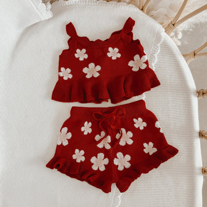 Red children's outfit with white flower patterns on a white surface