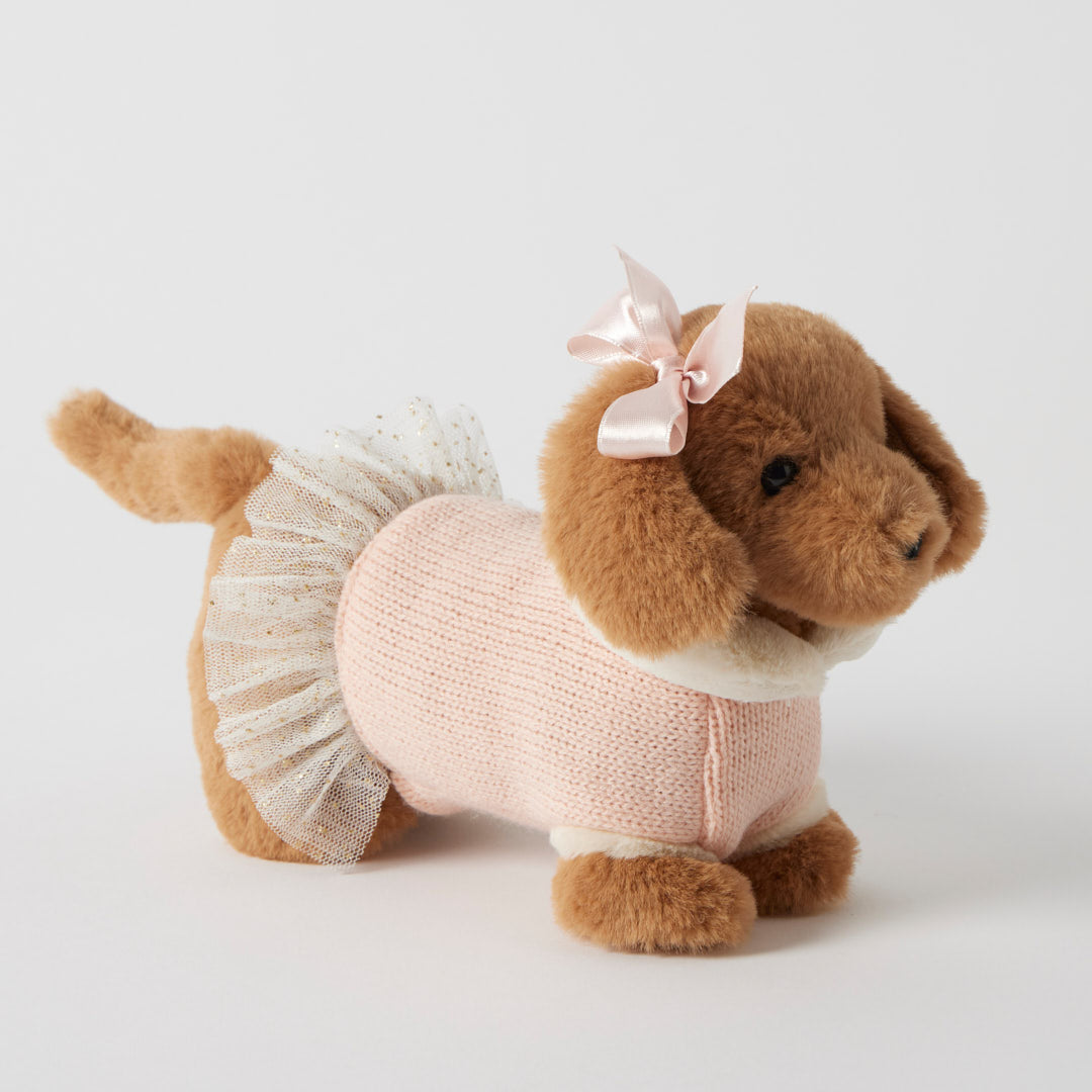 Stuffed dog toy wearing a pink sweater and white skirt with a bow on a light gray background