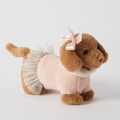 Stuffed dog toy wearing a pink sweater and white skirt with a bow on a light gray background