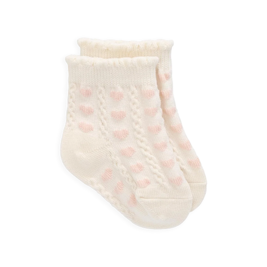 Cream-colored baby sock with pink polka dots on a white background