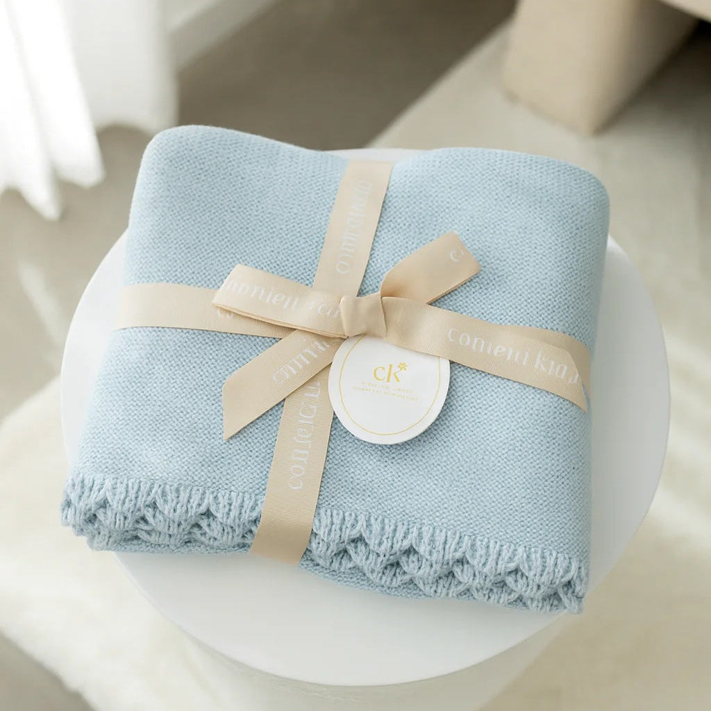 Light blue blanket with a beige ribbon on a white surface