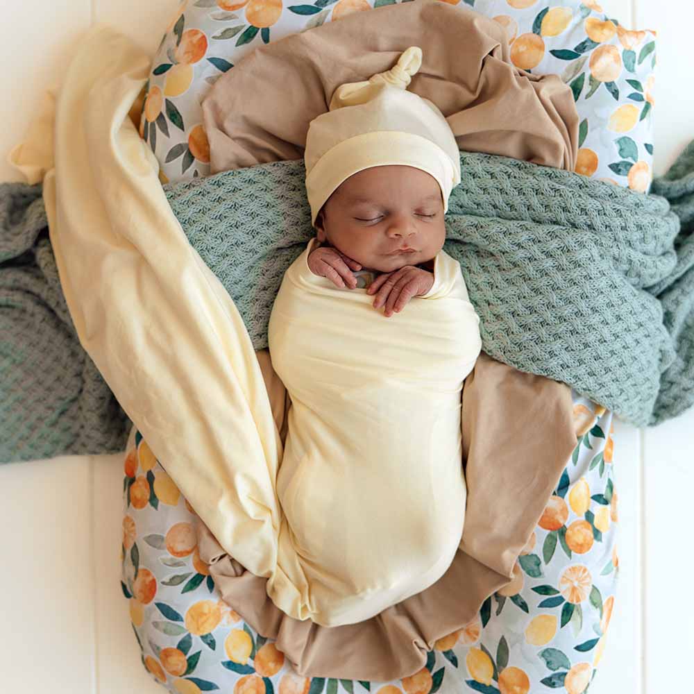 Newborn baby wrapped in beige swaddle with matching hat, lying on a floral-patterned blanket.